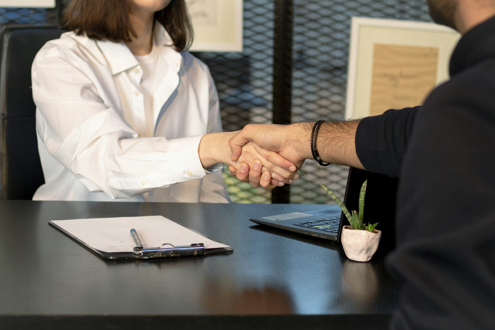 Two people shaking hands over paperwork at a desk